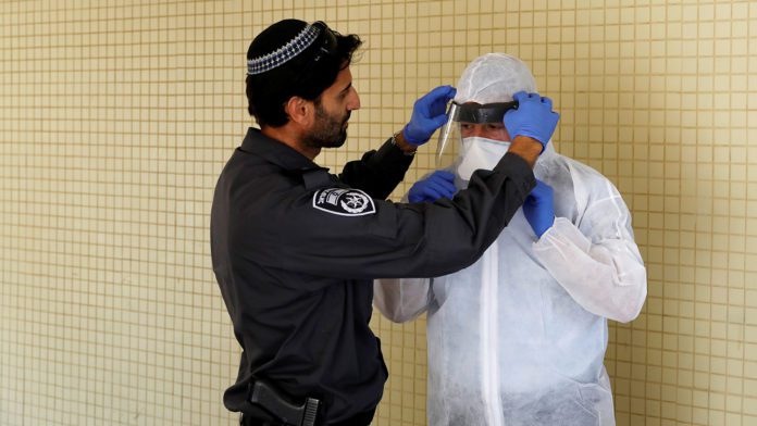 An Israeli police officer helps a Health Ministry inspector put on protective gear before they go up to the apartment of a person in self quarantine as a precaution against coronavirus spread in Hadera