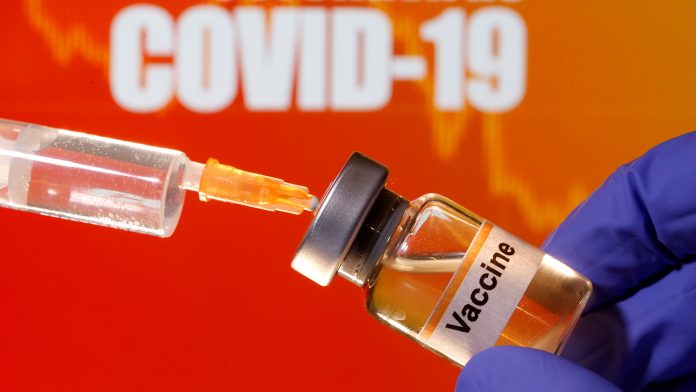 FILE PHOTO: A small bottle labeled with a "Vaccine" sticker is held near a medical syringe in front of displayed "Coronavirus COVID-19" words in this illustration